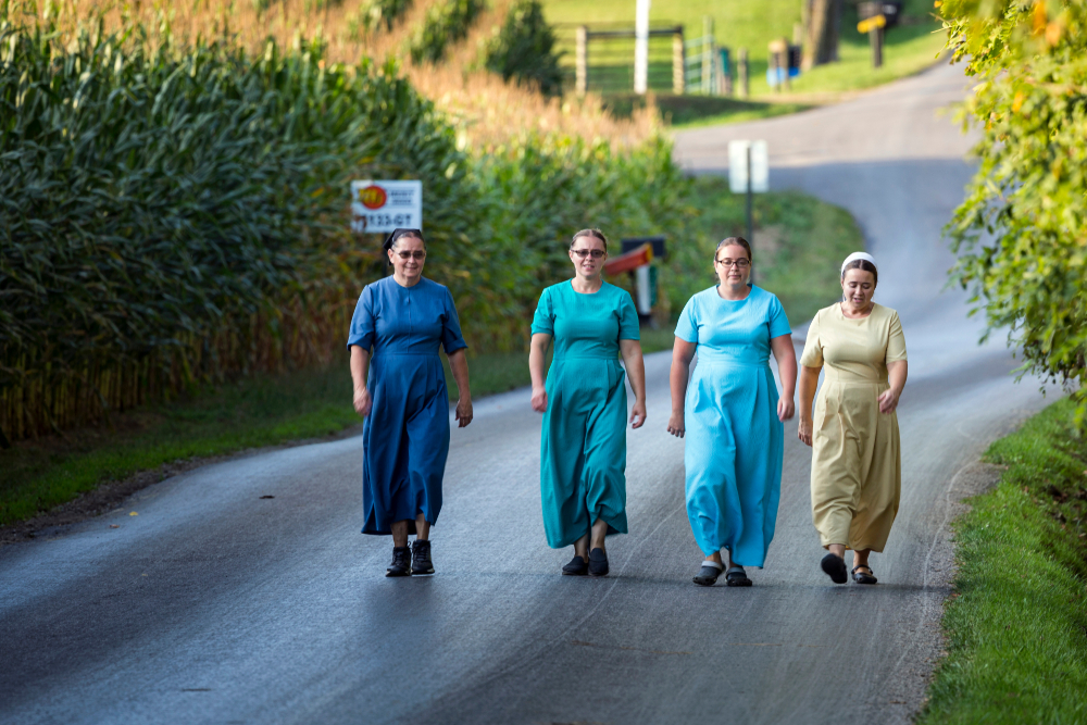 Four Amish Country Ohio women walking down rural road light blue dresses.
