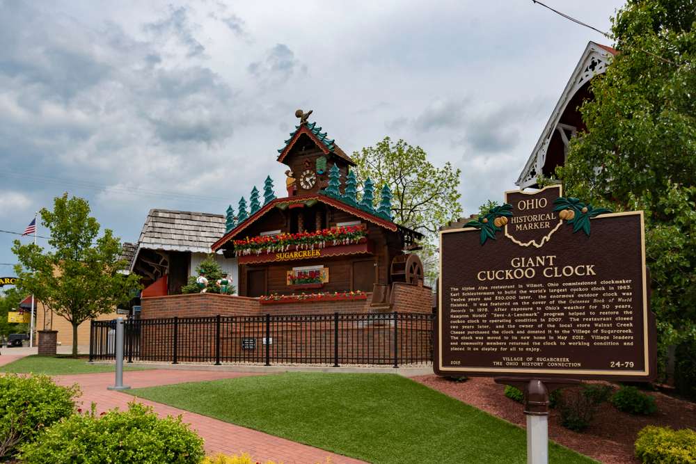 Ohio historical marker in Amish Country Ohio explaining giant cuckoo clock with German-inspired building in background.