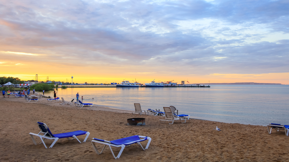 Mackinac City beach in Michigan with blue beach chairs and calm waters and sandy beach.