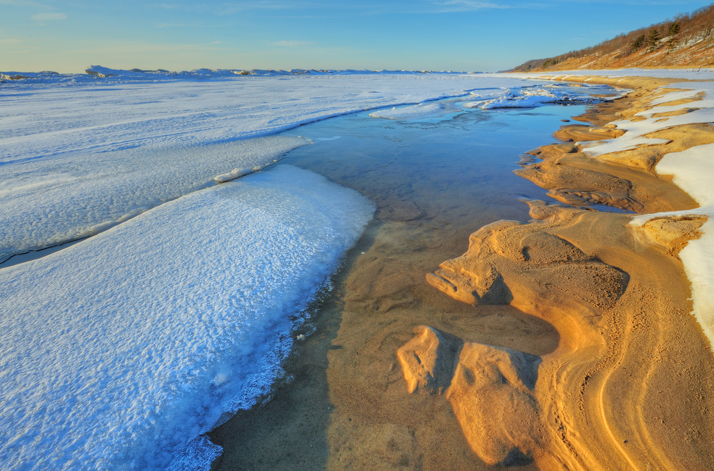 Saugatuck Dunes in winter with rocky shoreline, and snow on beach.