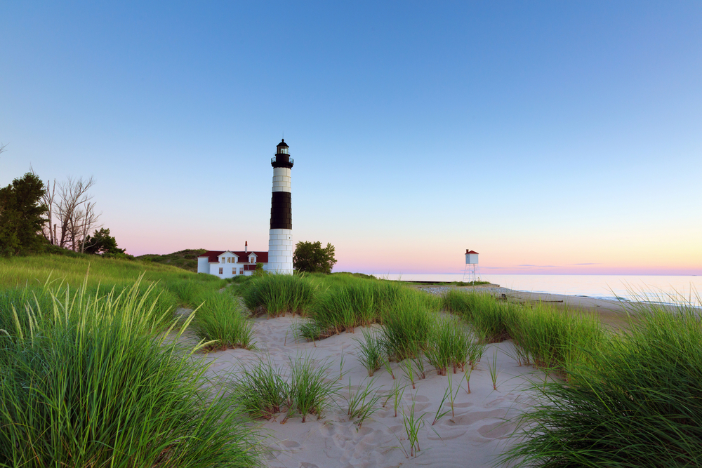 Michigan lighthouse with sandy beach and gorgeous sunset in background.