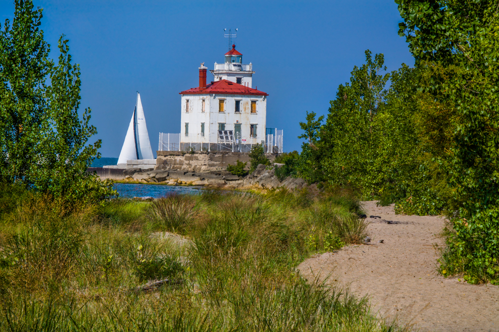 Sandy beach with green brush and red lighthouse with red roof in distance.