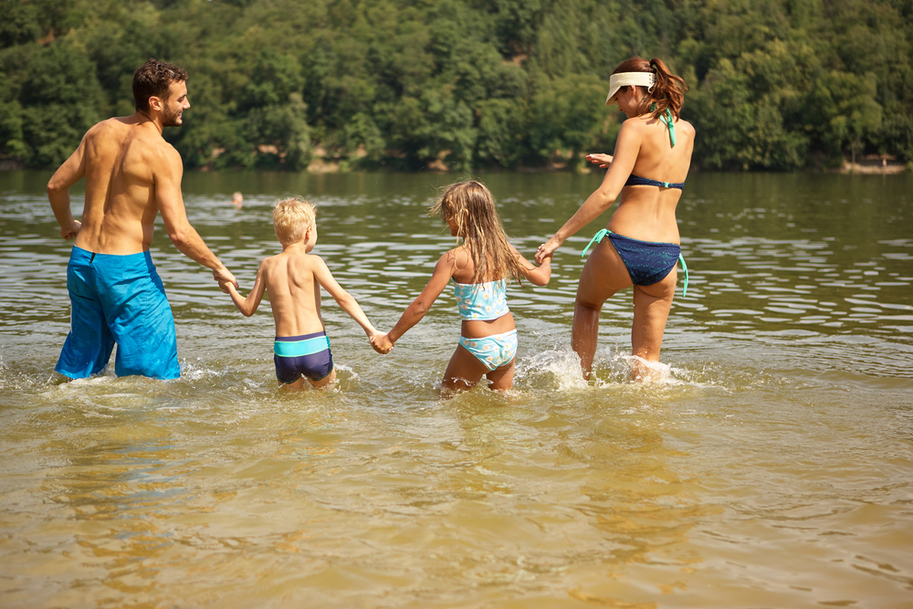 Family of 4 splashing and laughing in lake waters.