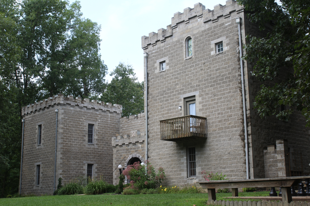 Gray stone castle in Ohio with wooden balcony among green trees.