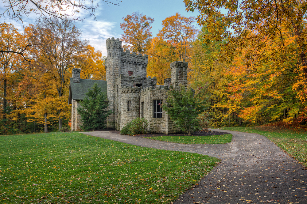 Photo of romantic European-inspired gothic castle in Ohio surrounded by autumnal trees with a large green front yard.