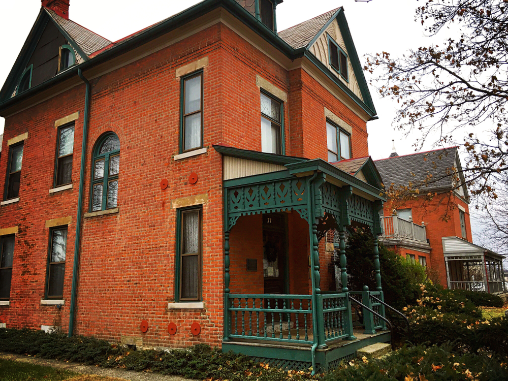 The Thurber House is one of the haunted Places in Ohio to visit. Photo of red brick house with green accents including ornate front porch.