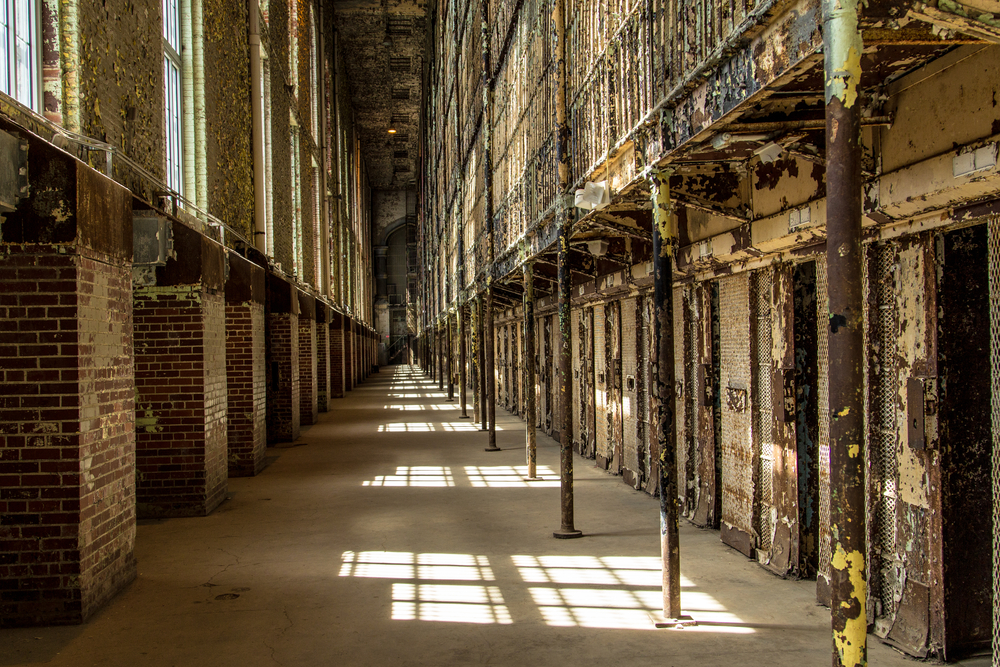 Dilapidated hallway of the Ohio State Reformatory with chipped paint and heavy doors of cells visible.
