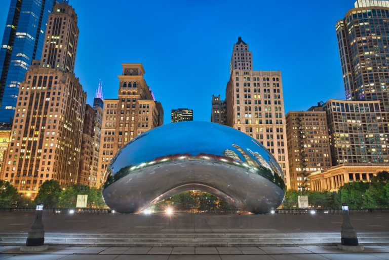 The silver Chicago Bean at twilight with illuminated Chicago skyline in background..