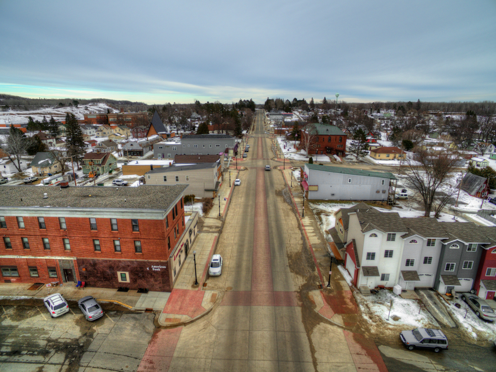 Small town Minnesota main street with red brick building in left foreground and colorful rowhouses in right foreground.