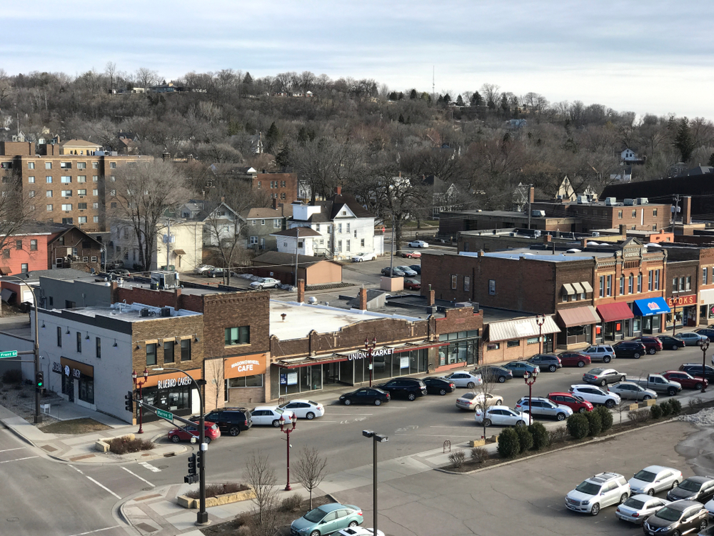 vintage downtown Minnesota with storefronts and cars parked and hills in background.
