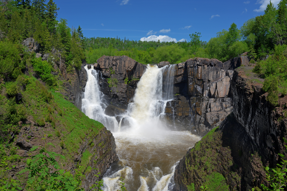 Thundering waterfall cascading over large rocks down into water below.