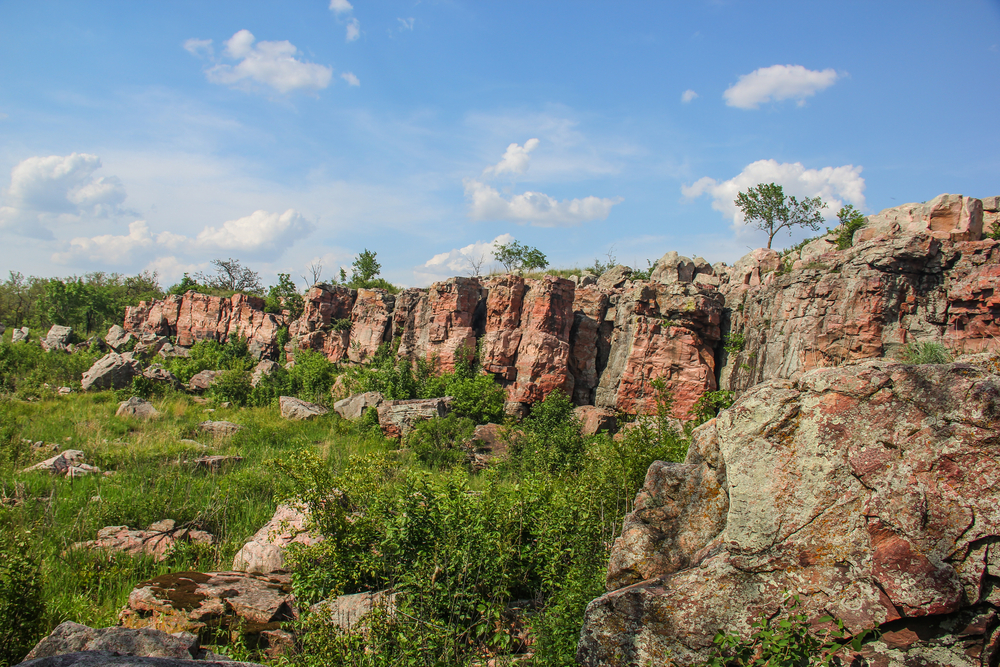 Pink Sioux Quartzite ridgeline in small town Minnesota with green brush in front of it and blue skies.