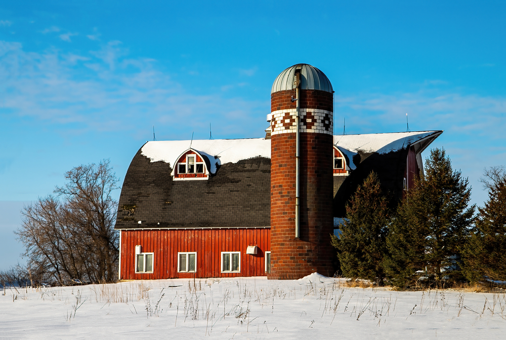 A red barn in Minnesota small town that has a quilt pattern in the bricks of the silo with snow in the foreground.