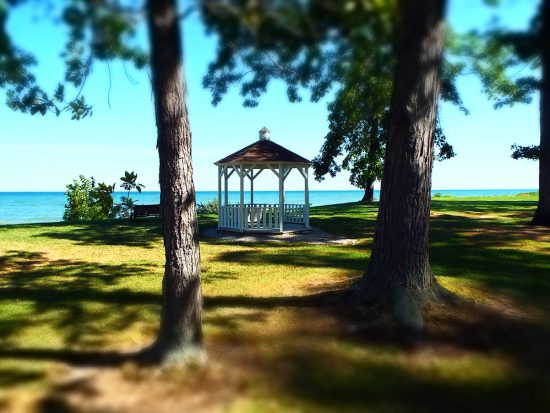 White gazebo located in park in Geneva-on-the-Lake, small town Ohio, with blue waters of Lake Erie in background.