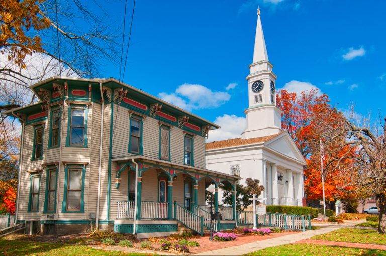 Vintage house, brown with green accents, sits next to white church with steeple in Twinsburg. Small town in Ohio