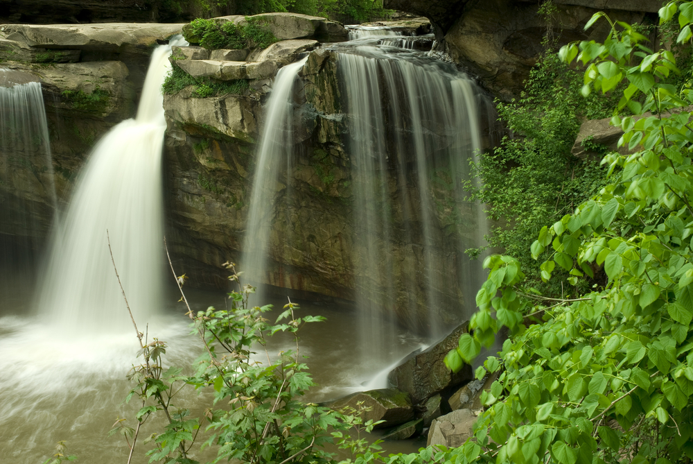 Cascading waterfall in Ohio rushed over large rock formations info water below. Green tree in foreground.