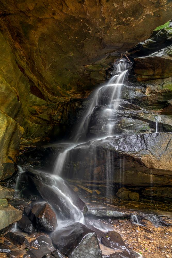 Water running down crevices in rock wall to very shallow pool with rocky bottom.