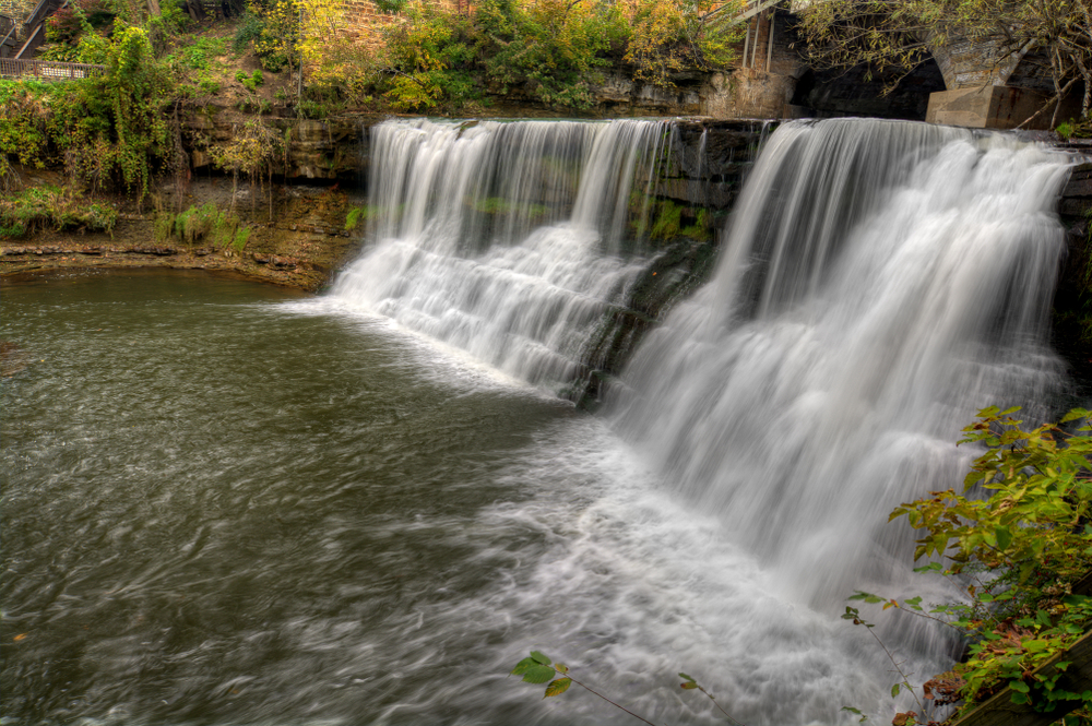 Chagrin waterfalls in Ohio - two cascading falls over rocks with trees and stone bridge in background.