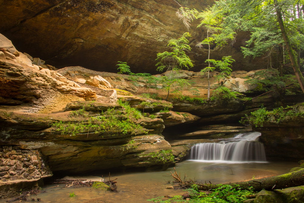 Small waterfalls pouring out over rocks into small pool of water. in background large rock formations.