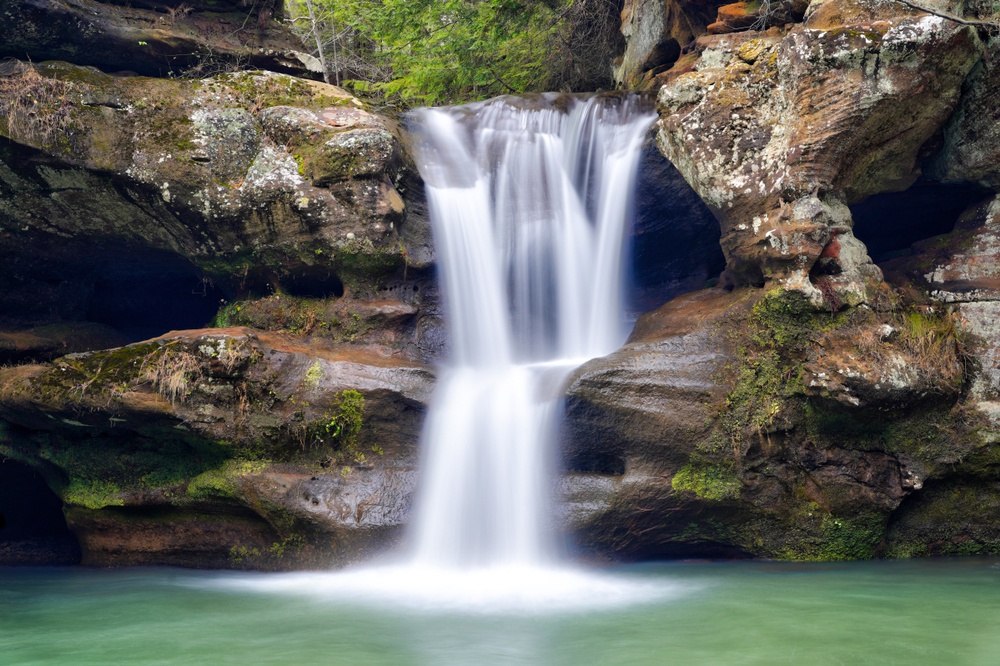 Water cascading down through rocks into pool of green water below