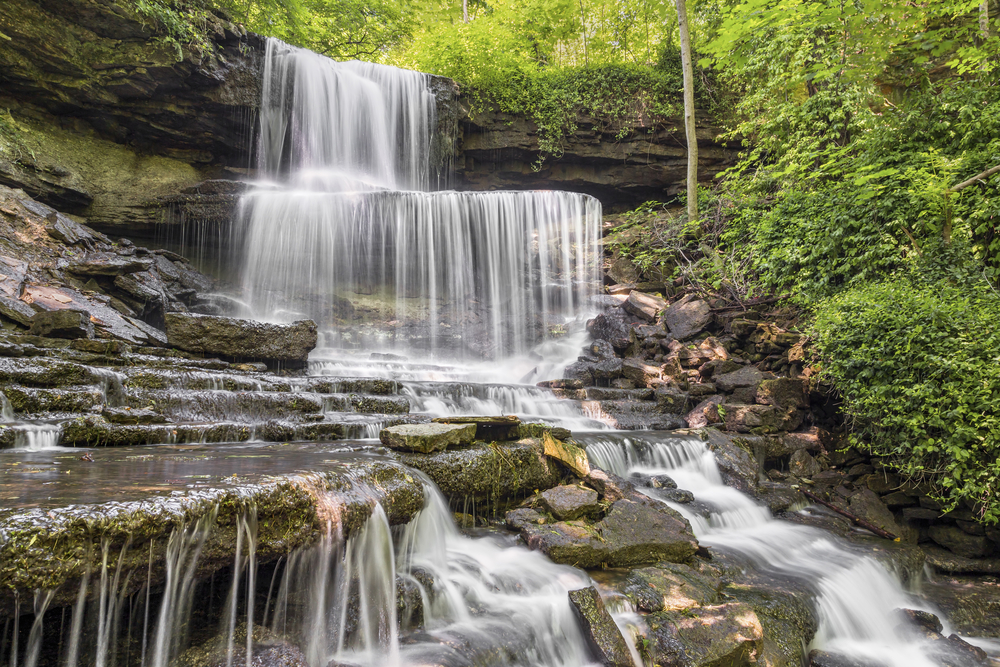 Several layers of water cascading over rock ledges with green trees in background.