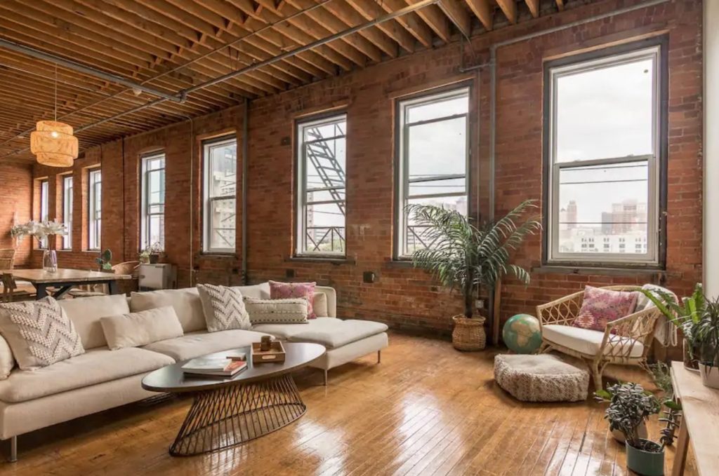 A large loft space with plenty of windows, exposed brick walls, exposed wood beam ceilings, and neutral decor in Detroit Michigan one of the best Airbnbs in the Midwest