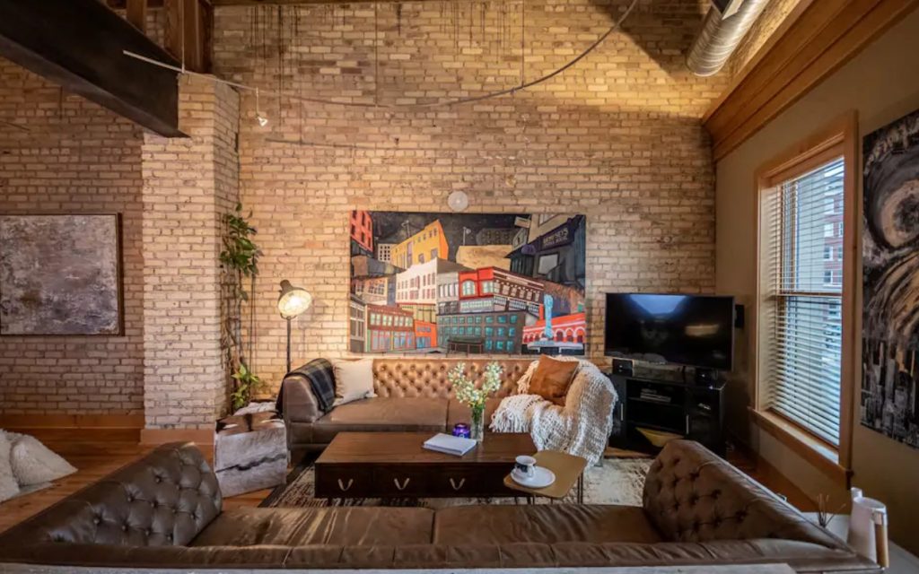 The living room of a large condo in Fargo North Dakota with tall ceilings, exposed brick walls, original art, and leather sofas one of the best Airbnbs in the Midwest