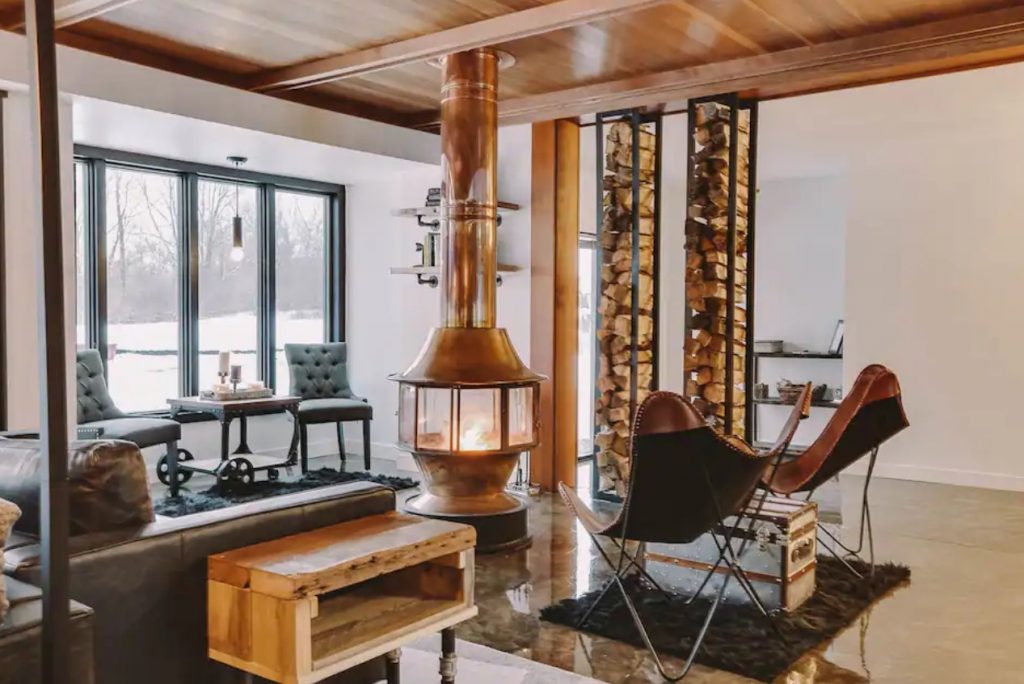 The inside of a modern home's living area with leather couches and chairs and a large copper wood burning fireplace one of the best Airbnbs in the Midwest