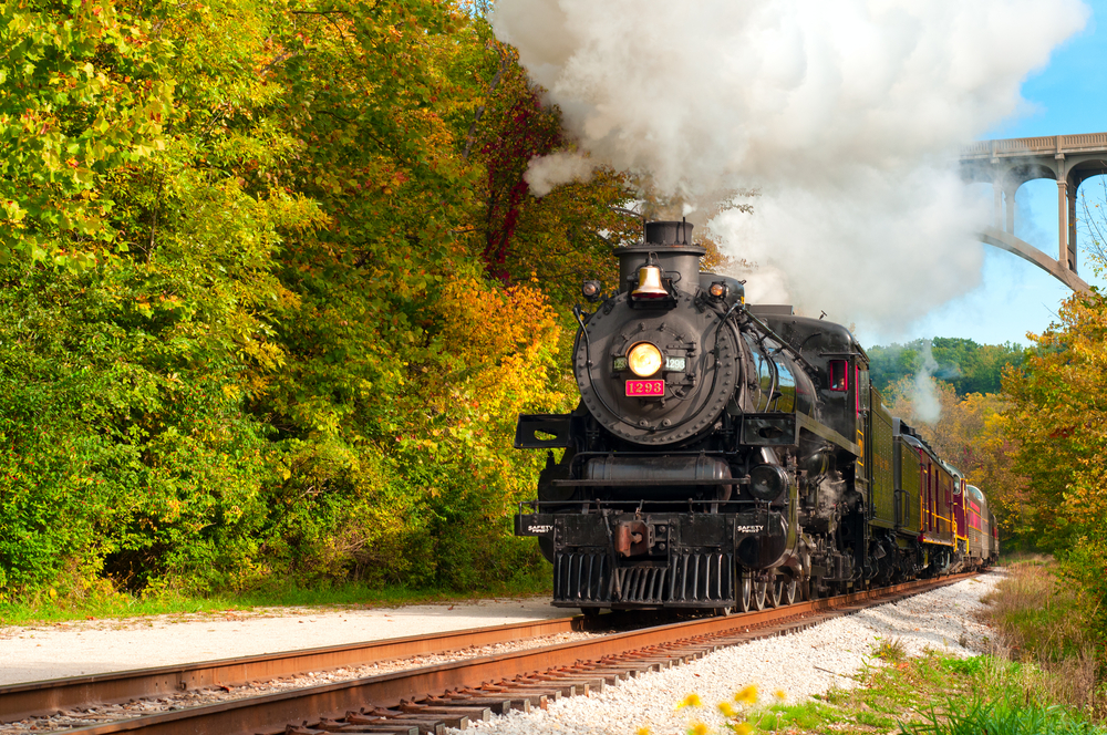 Black engine of passenger train in Cuyahoga Valley National Park with green trees on either side of the tracks.