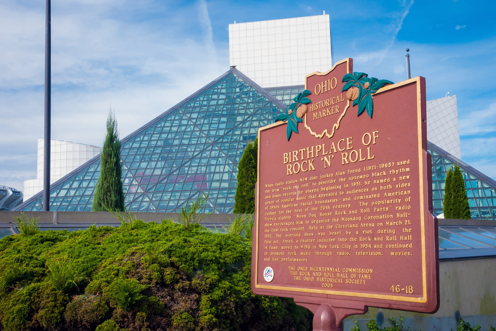 Brown Ohio historical marker explaining the Rock & Roll Hall of Fame with the glass pyramids in the background.