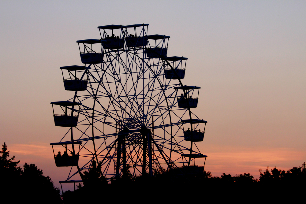 A Ferris wheel against a sunset sky with trees below in an article about amusement parks in the Midwest