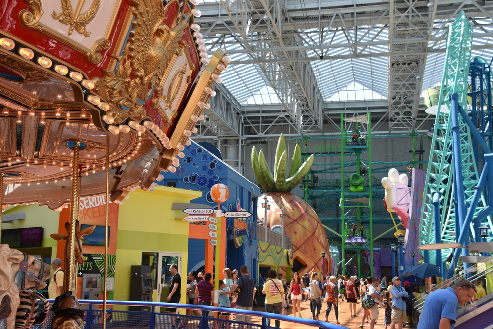 People in an amusement park with a carousel in the foreground and a giant pineapple in the background