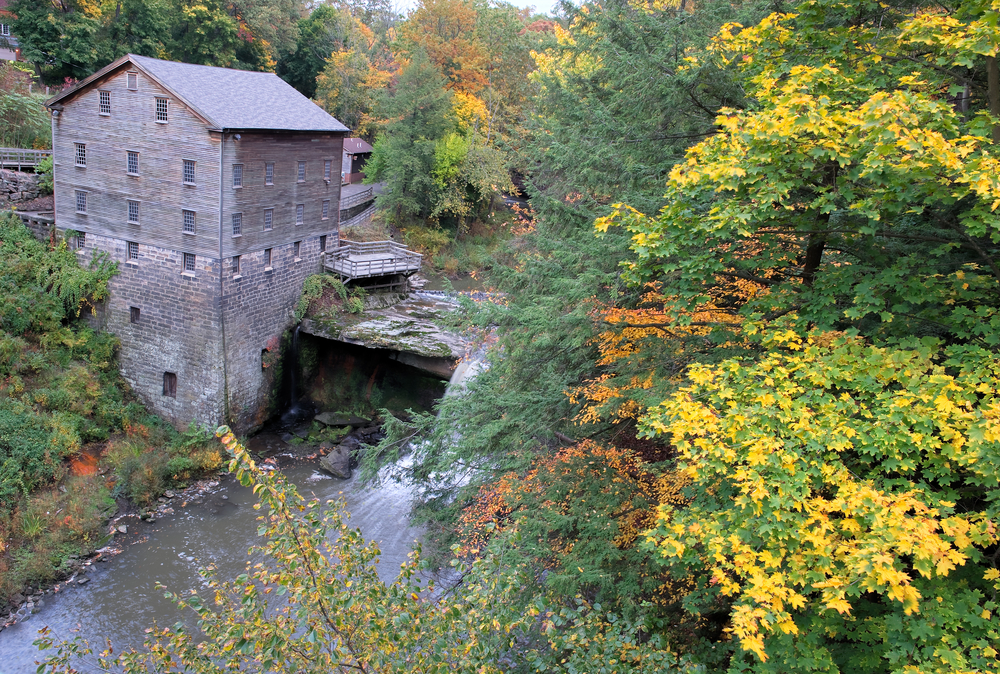 Brick building with deck next to rushing river surrounded by autumnal trees.