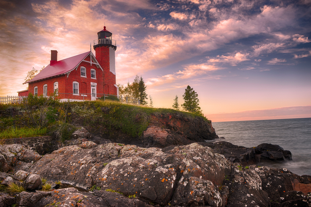 Sunset over a large red lighthouse on the rocky edges of Lake superior
