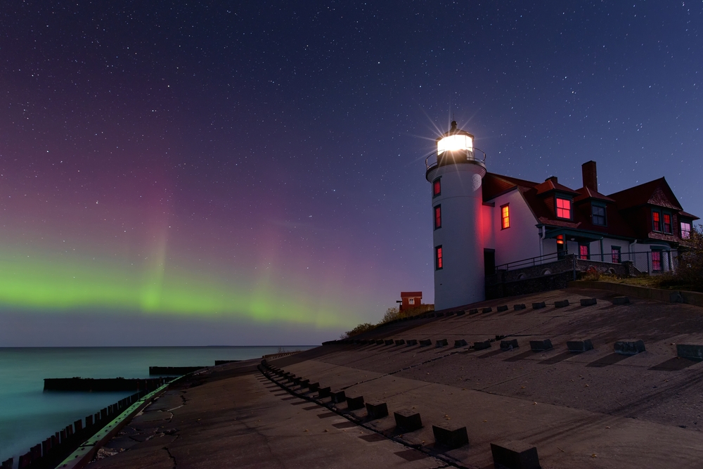 White lighthouse in Michigan with red roof, illuminated from within. Northern Lights in sky background.