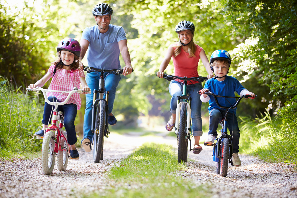 Family of 4, mom, dad, daughter, son enjoying biking outdoors on path with green trees around them. Fun thing to do in Hocking Hills.