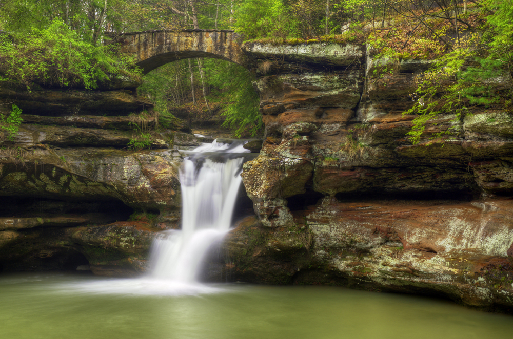 A cave waterfall in Hocking Hills spilling over rock formation into pool of water. one of the things to do in Athens, Ohio