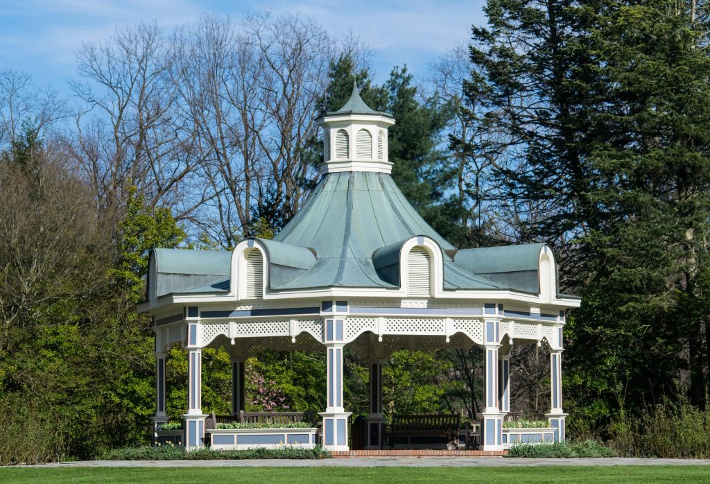 Pretty white gazebo with ornate trim and green roof. 