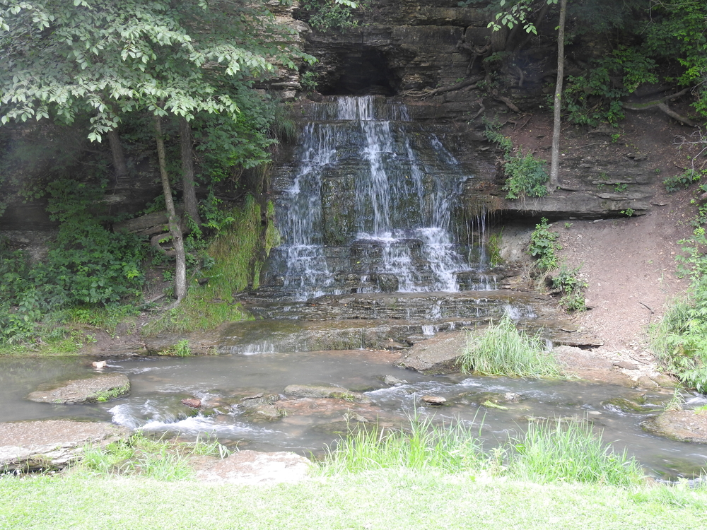 A waterfall tumbling over the rockface. Spook Cave is in the background one of the caves in Iowa