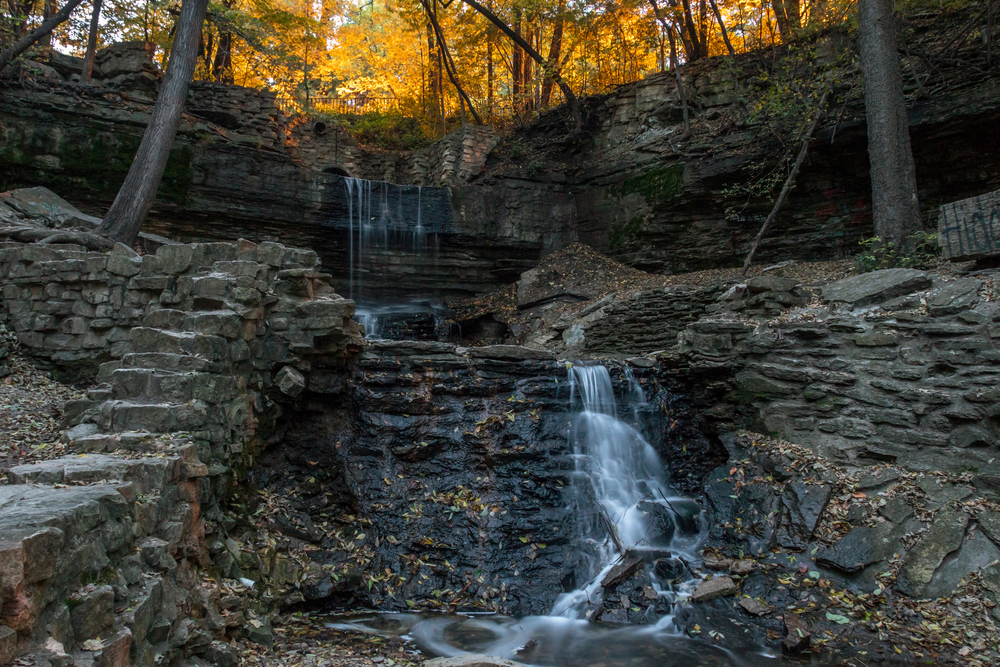 An urban waterfall in St. Paul Minnesota that goes down stone steps with fall trees in the background