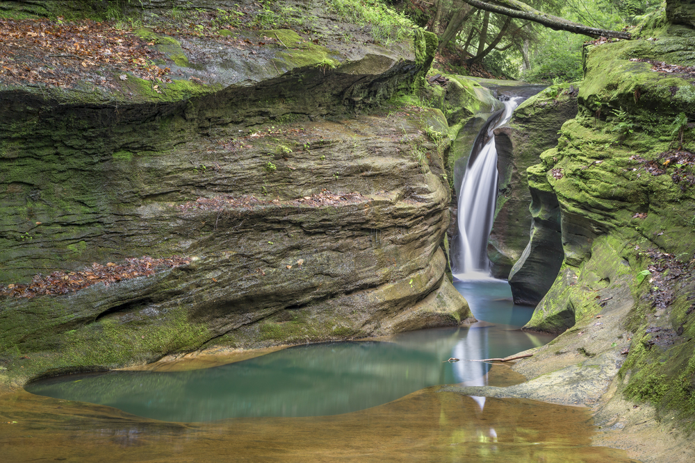 a rock pool surrounded by rocks with a waterfall in the background.