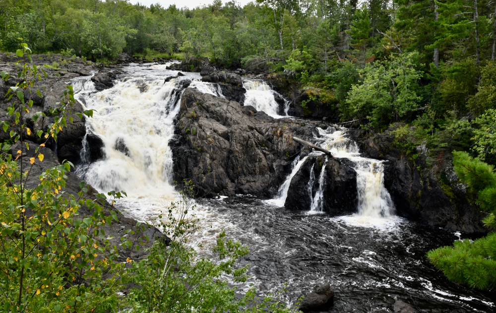 A large waterfall that spreads over several rocky portions of the cliffside surrounded by lush greenery waterfalls in minnesota