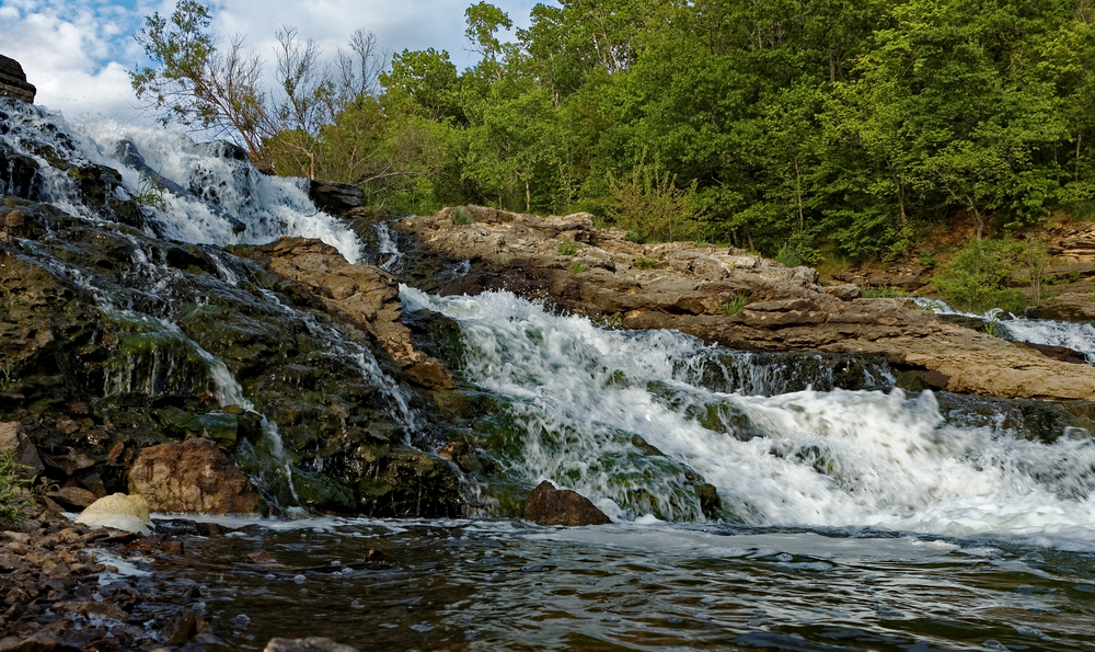 Water rushes over the Lake MacBride Waterfall. Trees are in the background