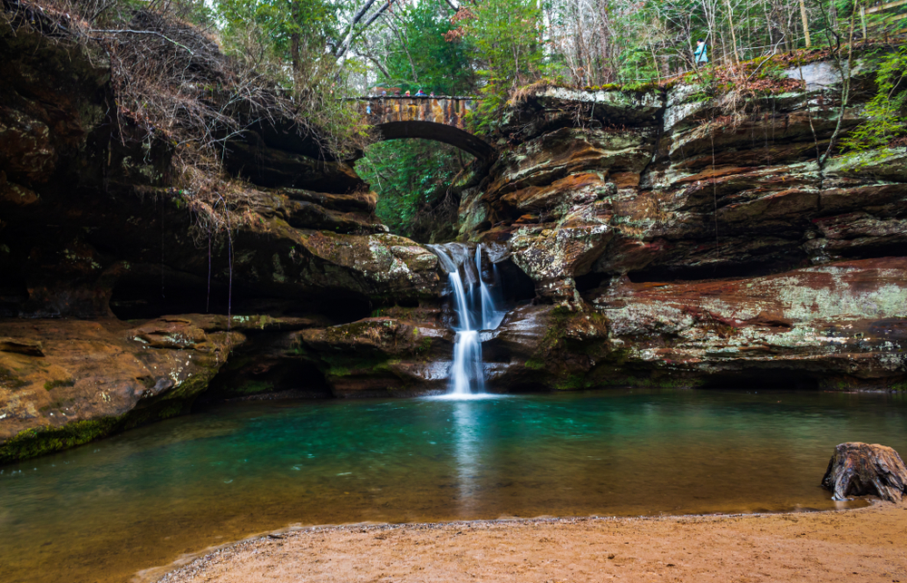 Waterfalls cascading down brown rock formations into pool of water below are one of the fun things to do in Hocking Hills Ohio.