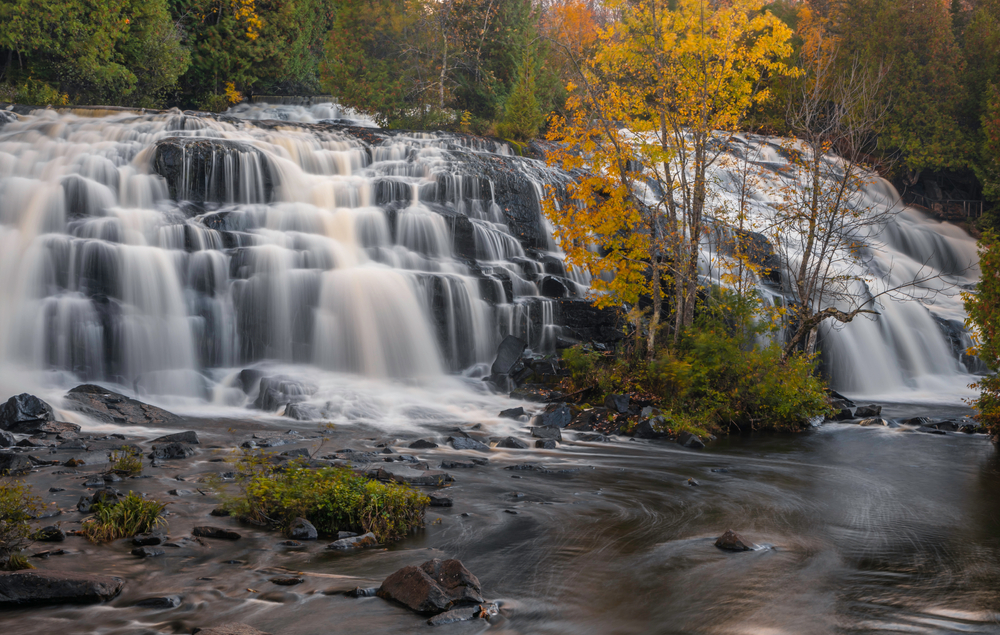 The incredible Bond Waterfalls in Michigan. Its a rock step fall and there is a tree in the foreground.