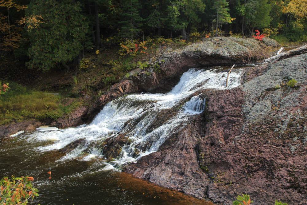 Water tumbling over a large rock with a forest in the background Great Conglomerate is one of the waterfalls in Michigan