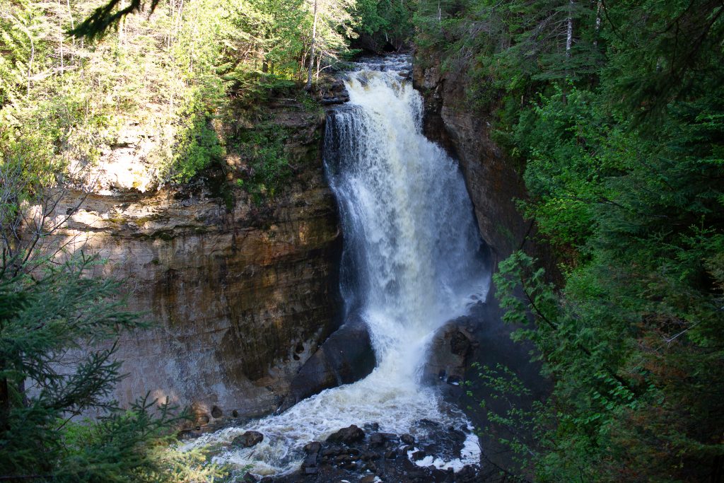 Munising waterfalls in Michigan . It's a large fall tumbling off a cliff with foliage around the cliff.