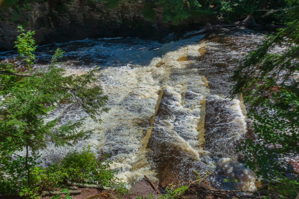 A small wide step waterfall running into a large river .