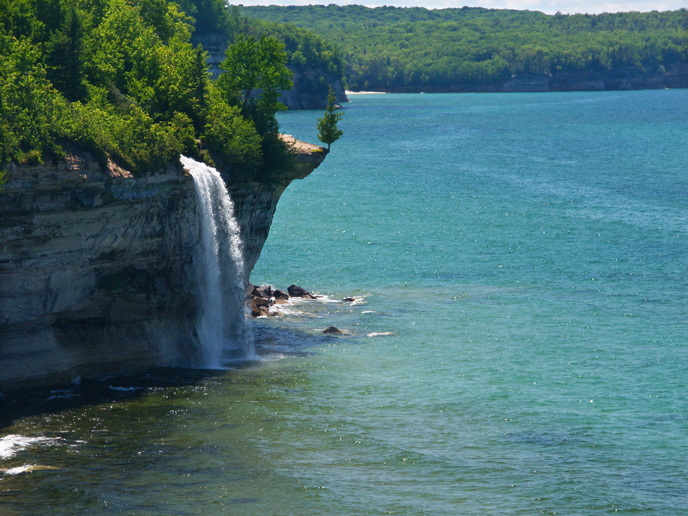 A waterfall tumbling from a tree lined cliff into a large lake below.