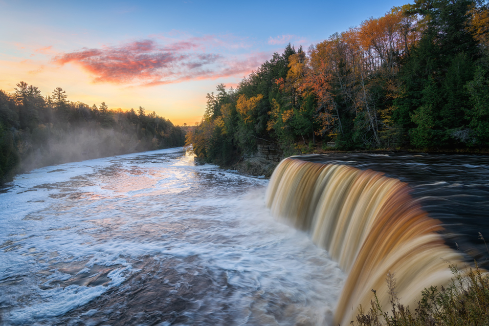 A large waterfall in the foreground with fall foliage in the background